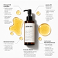 A bottle of Juóda Kópa facial wash centered on a white background with callout text bubbles describing ingredients and benefits, surrounded by gold oil droplets.